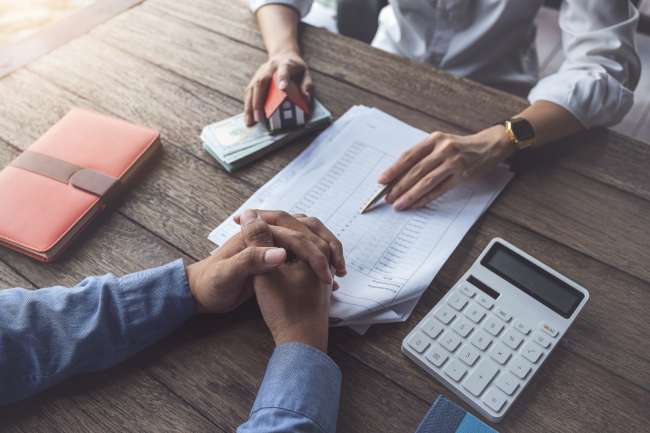 loan agreement, real estate agent or bank officer describes the loan interest to the customer, along with loan documents with a home style pen and a replica money on a wooden table.